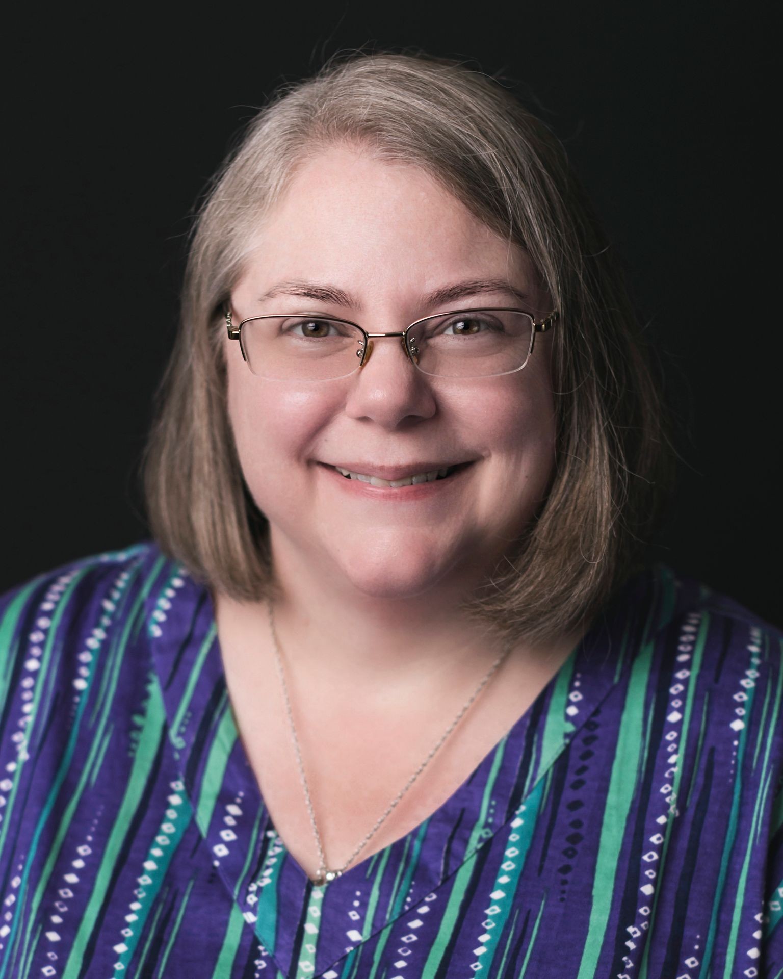 Person wearing a blue and green striped blouse with a silver necklace, set against a black background.