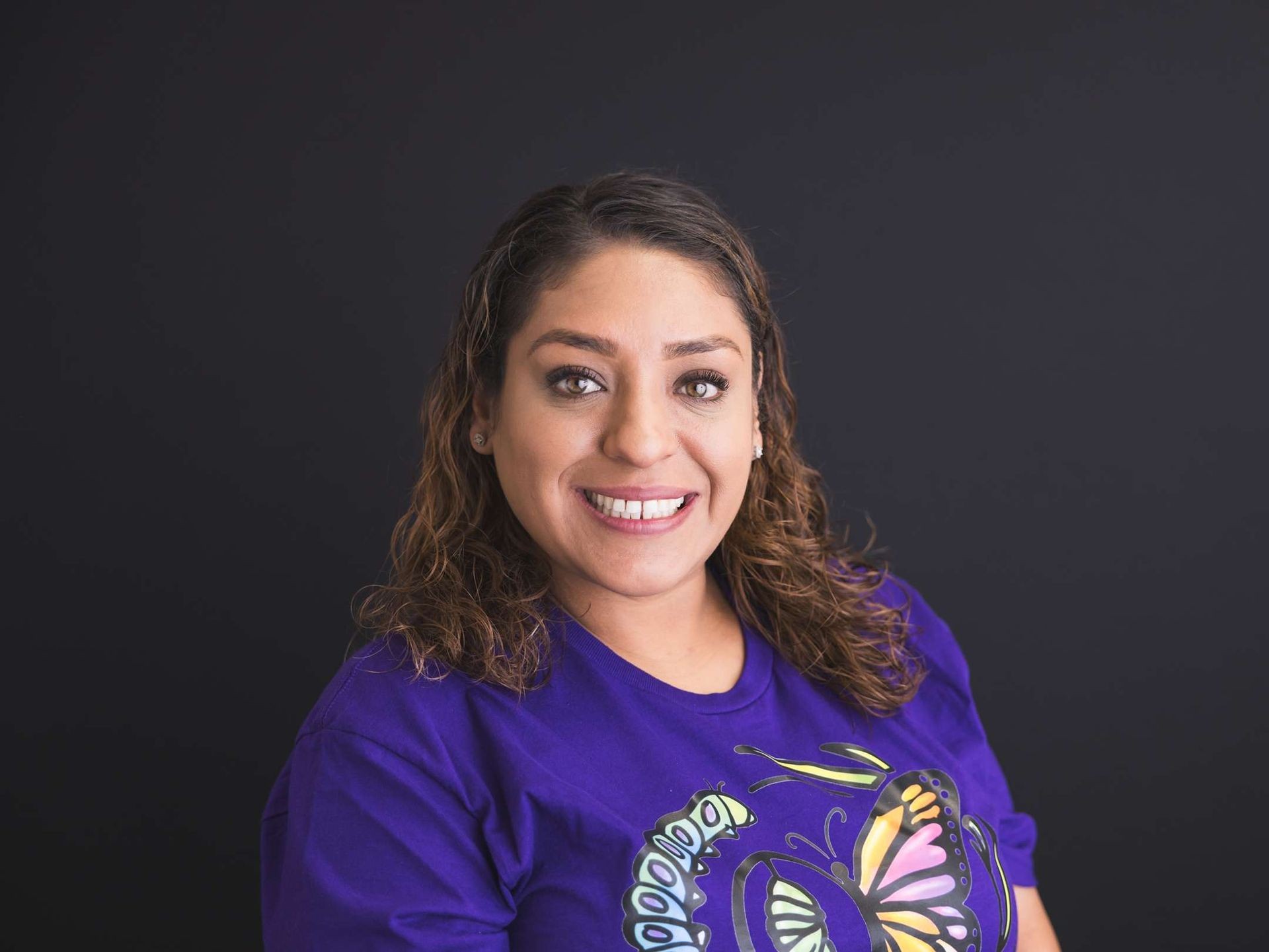 Smiling person in a purple shirt with a colorful butterfly design on a black background.