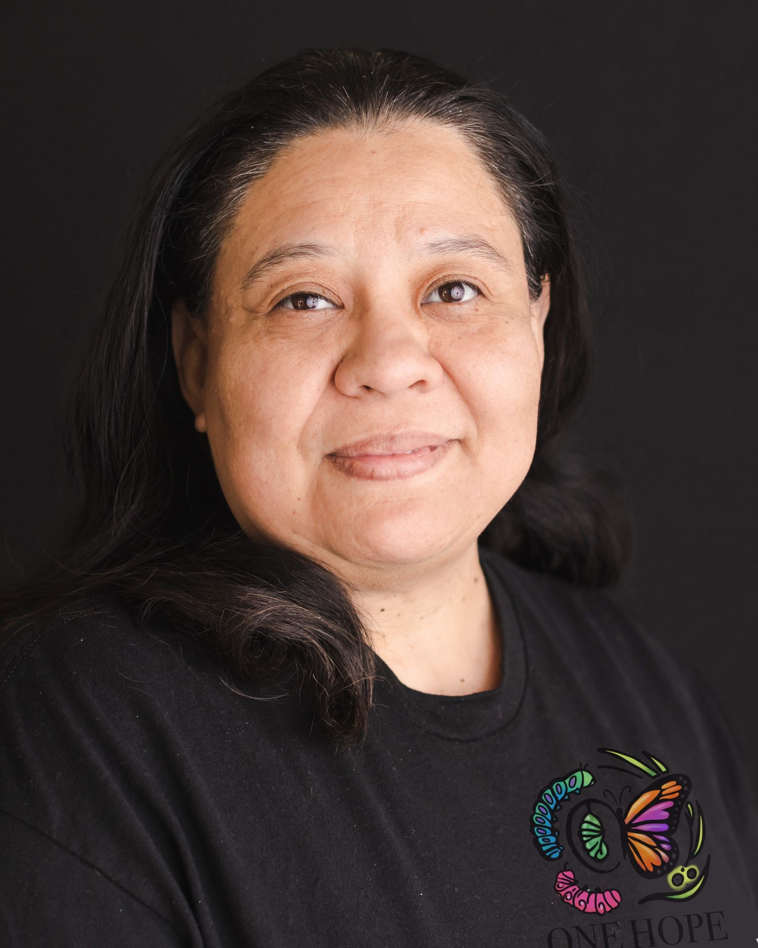 A woman with dark hair wearing a black t-shirt with a colorful butterfly logo.