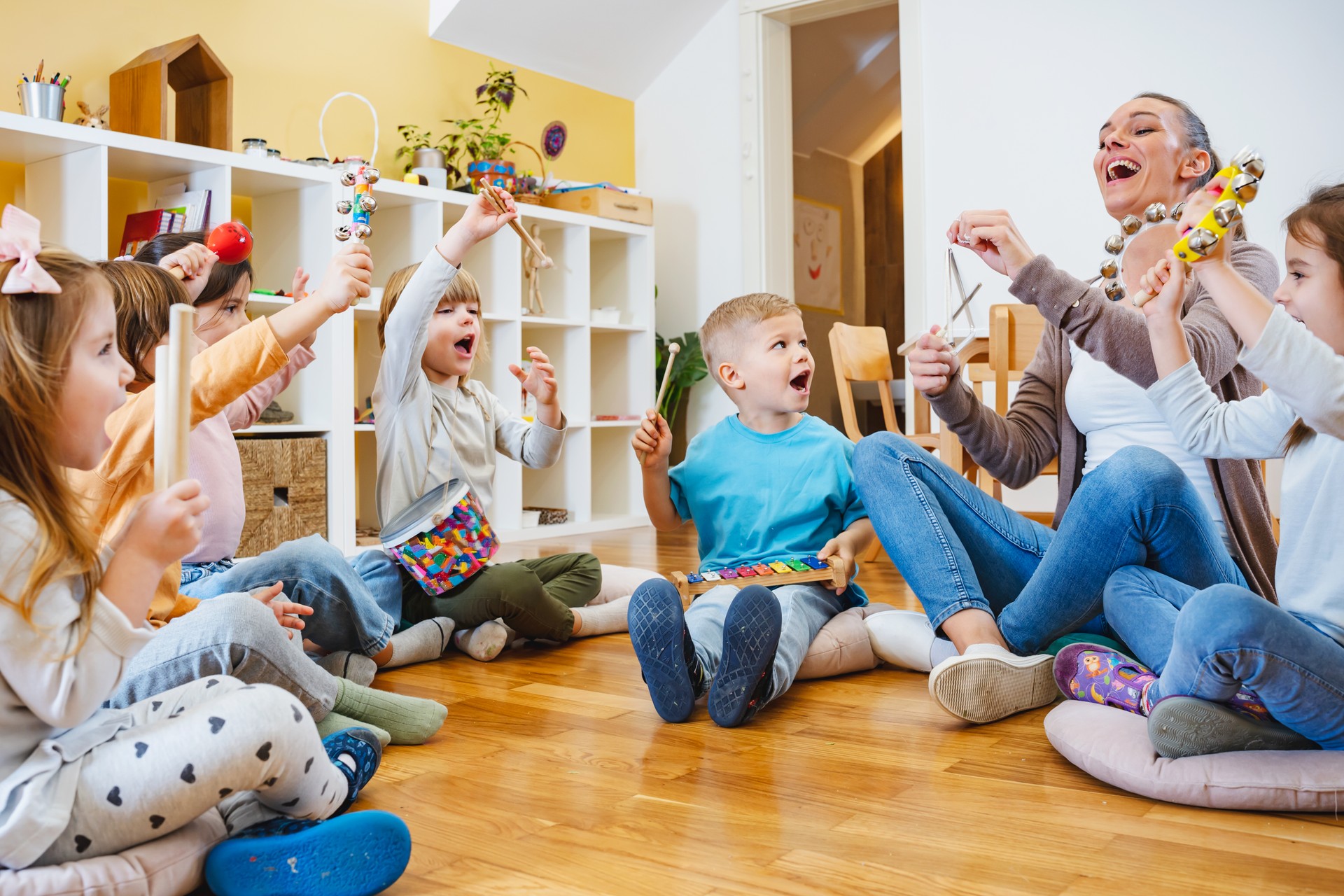 Kindergarten teacher with children sitting on the floor having music class, using various instruments and percussion.